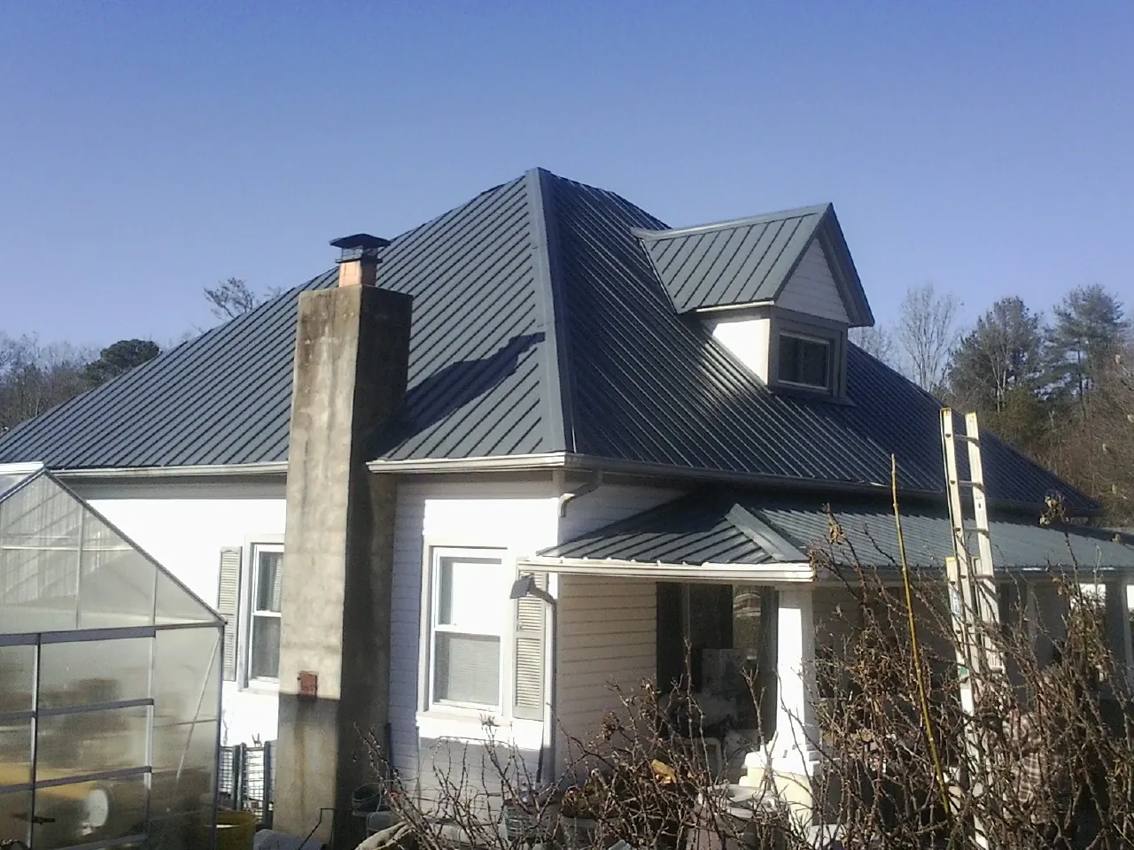 Dark blue standing seam metal roof on a white farmhouse with dormer — Slate & Tile Roof Repair by Roofing Brothers in Damon