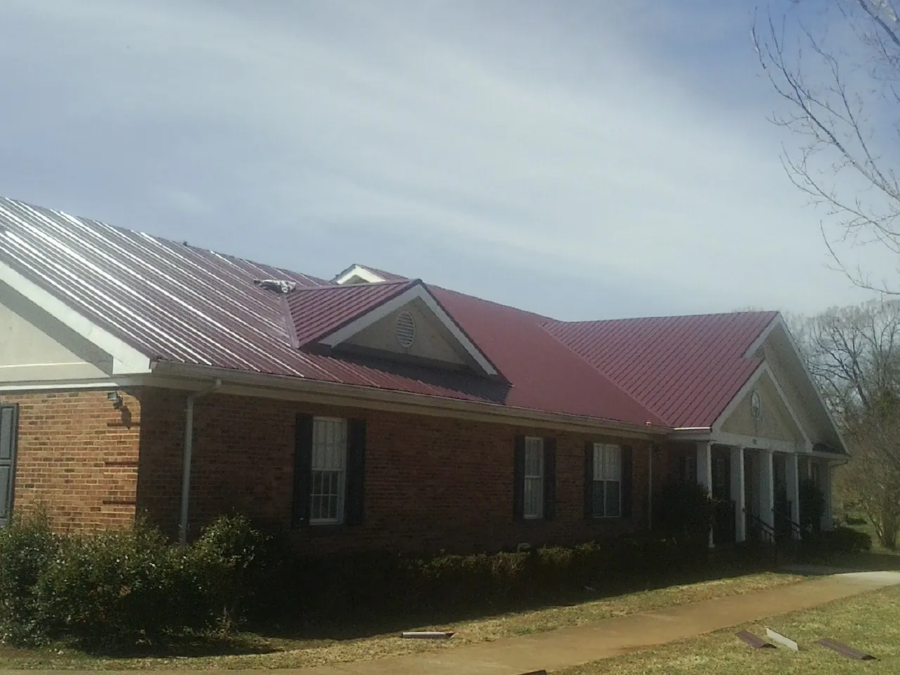 Red metal roof with gabled entries on a long brick building, from a Hail Damage Roof Repair job in Damon