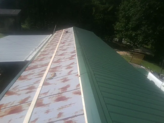 Old rusted panels beside newly installed green metal roofing — Wind Damage Roof Repair by Roofing Brothers in Damon