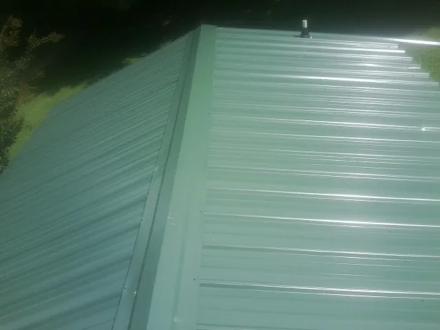 New green metal panels meeting at the ridge of a roof — Flat Roof Repair work by our crew in Damon
