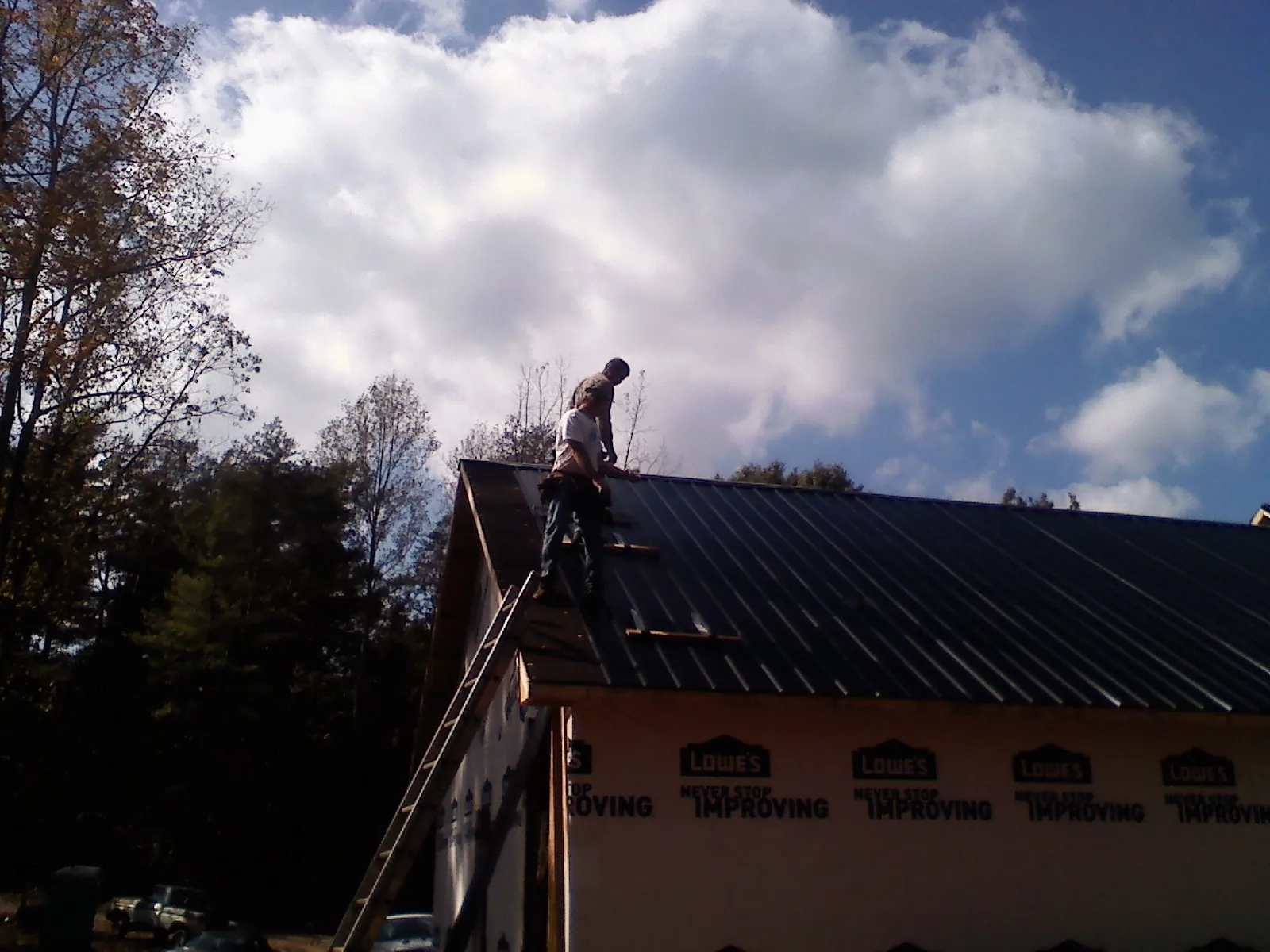 Roofer fastening dark metal panels high against a cloudy sky, from a Roof Inspection job in Damon