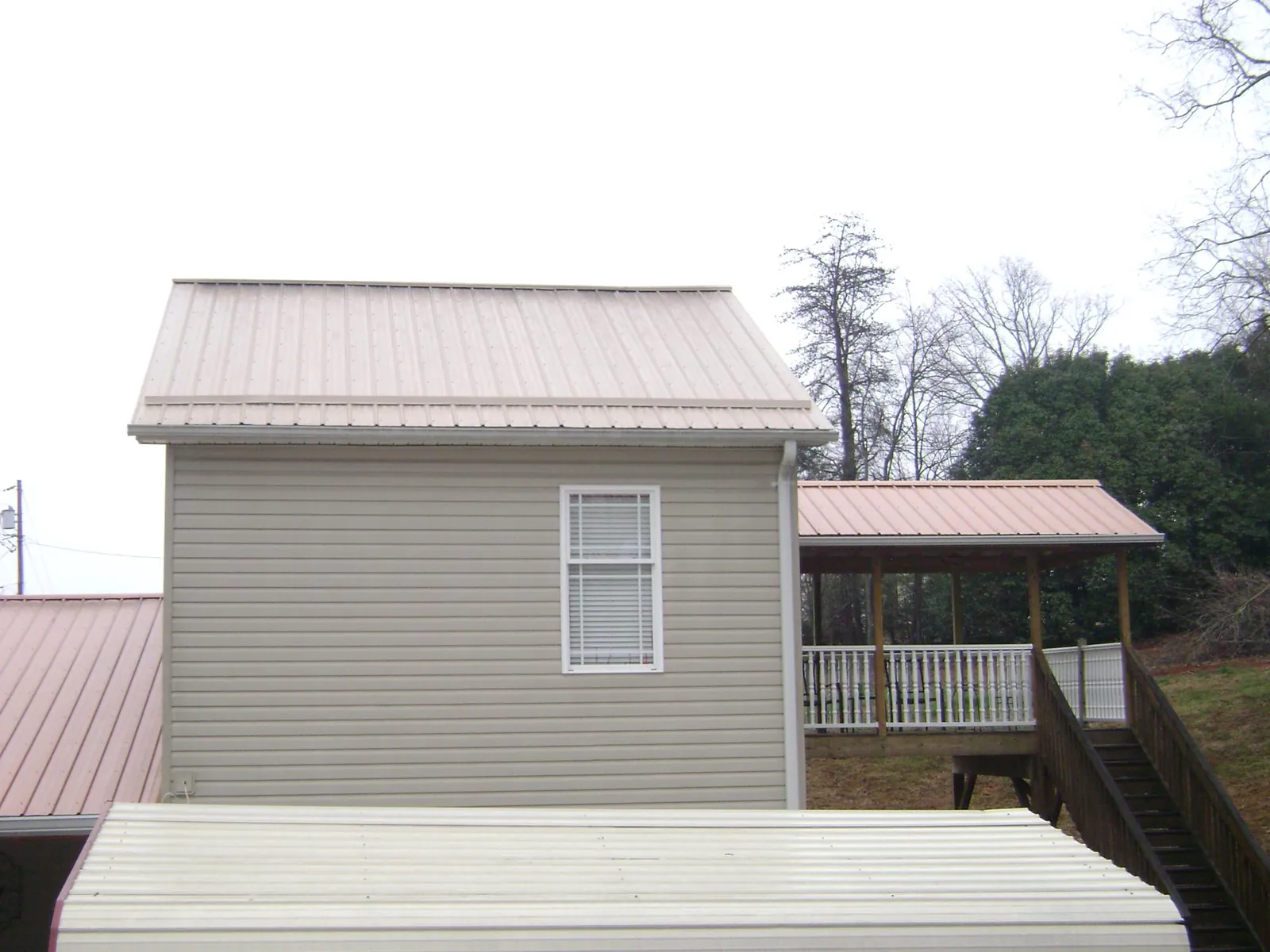 Tan metal roofs on a two story addition and attached porch, from a Roof Replacement job in Damon
